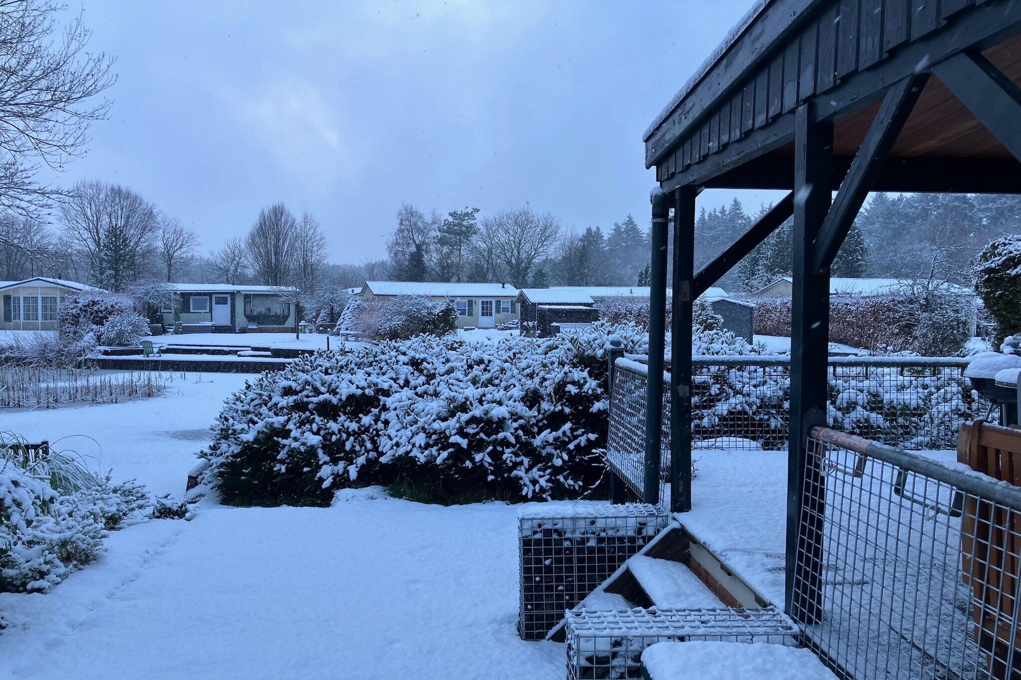 Un'area esterna innevata con una struttura in legno, probabilmente un balcone o un portico, e un recinto.