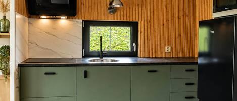 A kitchen with wooden paneling, a black TV, a window, and a black refrigerator.