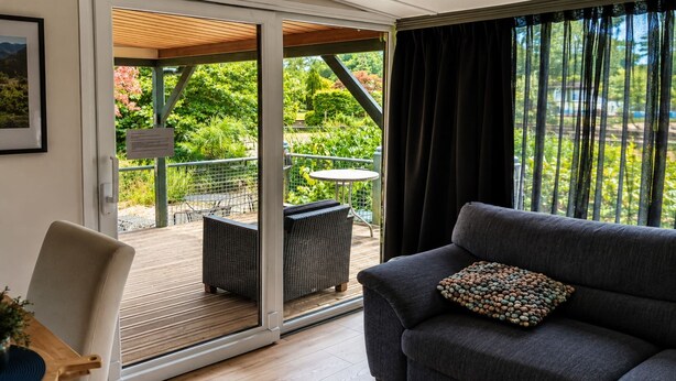Une pièce dotée d’une porte-fenêtre coulissante donnant sur un patio extérieur avec une table et des chaises, un canapé agrémenté d’un coussin décoratif et un tableau encadré accroché au mur.
