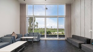 A spacious living room with a large window, grey sofas, a coffee table, and a view of greenery. - Diamond Blue Poll Villa D4bhk Luxurious Vegfood (Doddaballapur)