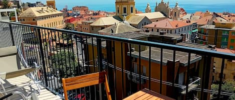 A balcony with a view of a coastal town, including buildings with domed roofs and a prominent church.