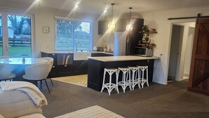 A modern kitchen with a central island, bar stools, and a dining area with a table and chairs. - Hamilton 3 bedroom Home overlooking paddocks 4 m from city (Tamahere)