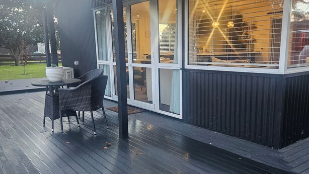 A covered outdoor area with a table and chairs, a potted plant, and a view of the interior through large windows. - Hamilton 3 bedroom Home overlooking paddocks 4 m from city (Tamahere)