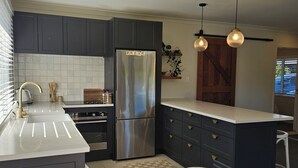 A modern kitchen with dark cabinets, stainless steel appliances, and pendant lighting. - Hamilton 3 bedroom Home overlooking paddocks 4 m from city (Tamahere)