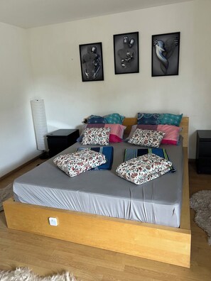 Une chambre à coucher avec un lit, des oreillers, une table de chevet, une lampe et trois œuvres d’art encadrées accrochées au mur.