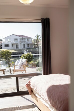 A bedroom with a large window, a bed, and a view of a building and greenery outside.