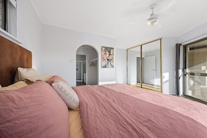 Une chambre à coucher comprenant un lit, un ventilateur de plafond, un tableau, une armoire et une porte-fenêtre coulissante.
