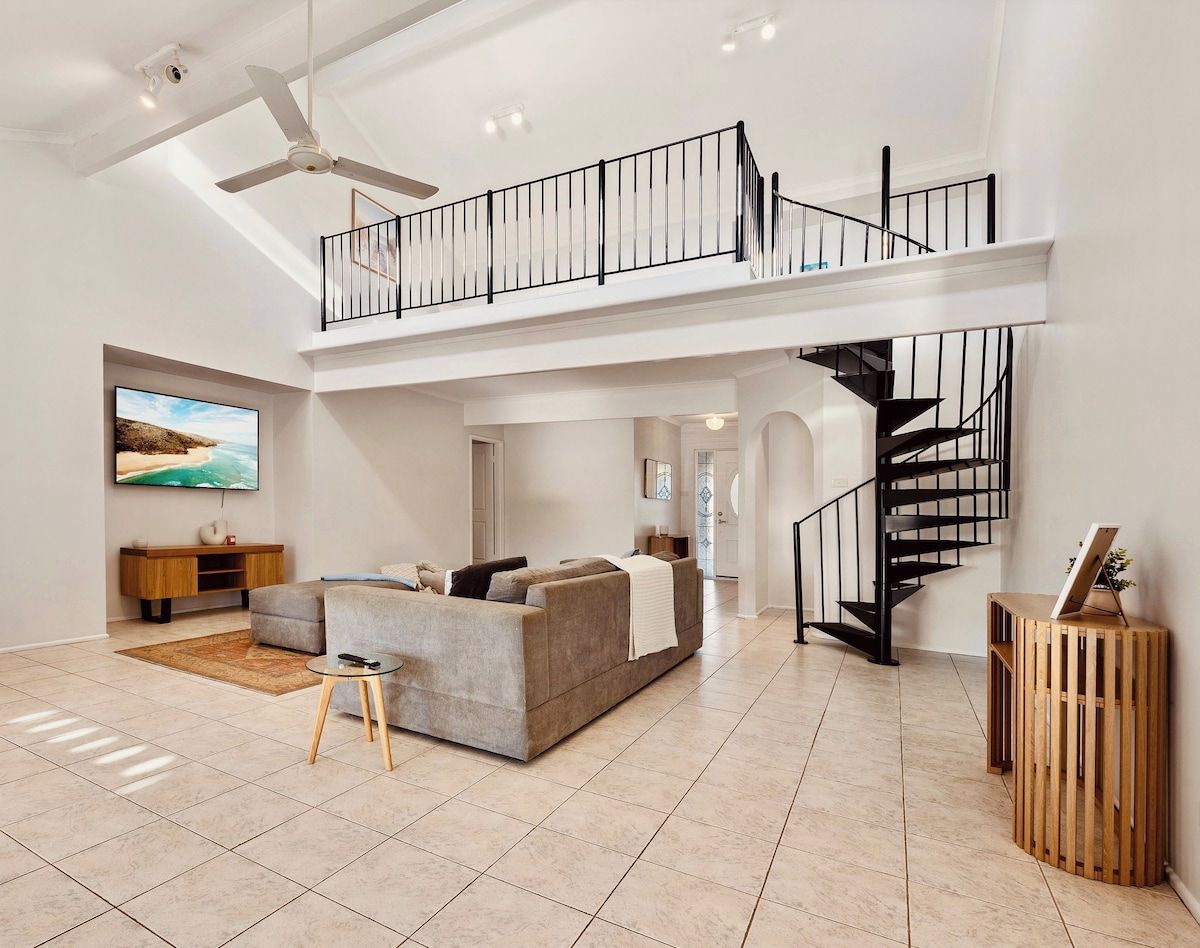 Un vaste espace de vie doté d’un haut plafond, d’un escalier moderne et d’un téléviseur à écran plat fixé au mur.