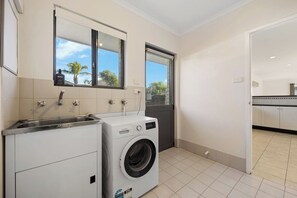 A laundry room with a washing machine, a sink, and a window with a view of palm trees.