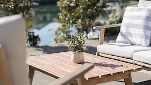 Eine Holzterrasse mit Tisch und Stühlen, einem Blumentopf und Blick auf ein Wohngebiet mit Häusern und einem Gewässer.