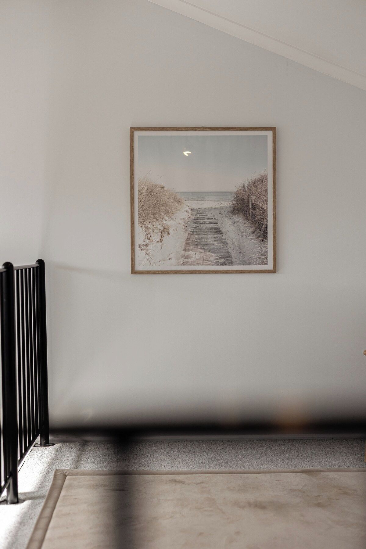 A hallway with a framed picture of a beach path, a radiator, and a carpeted floor.
