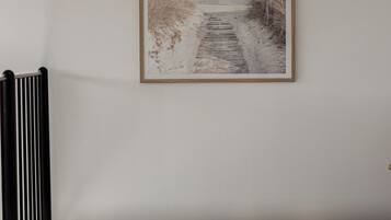 A hallway with a framed picture of a beach path, a radiator, and a carpeted floor.