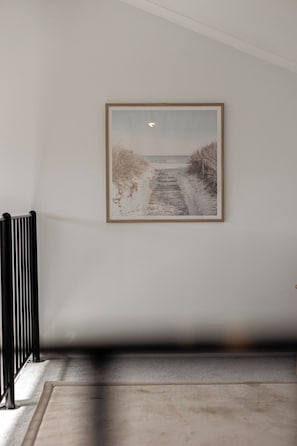 Un couloir avec un tableau encadré représentant un sentier de plage, un radiateur et un sol recouvert de moquette.