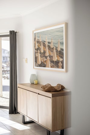 A room with a light wooden cabinet, a framed beach scene, and a window with curtains.