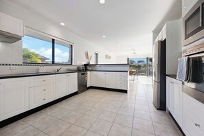 A modern kitchen with white cabinetry, a stainless steel refrigerator, and a large window providing a view of the outdoors.