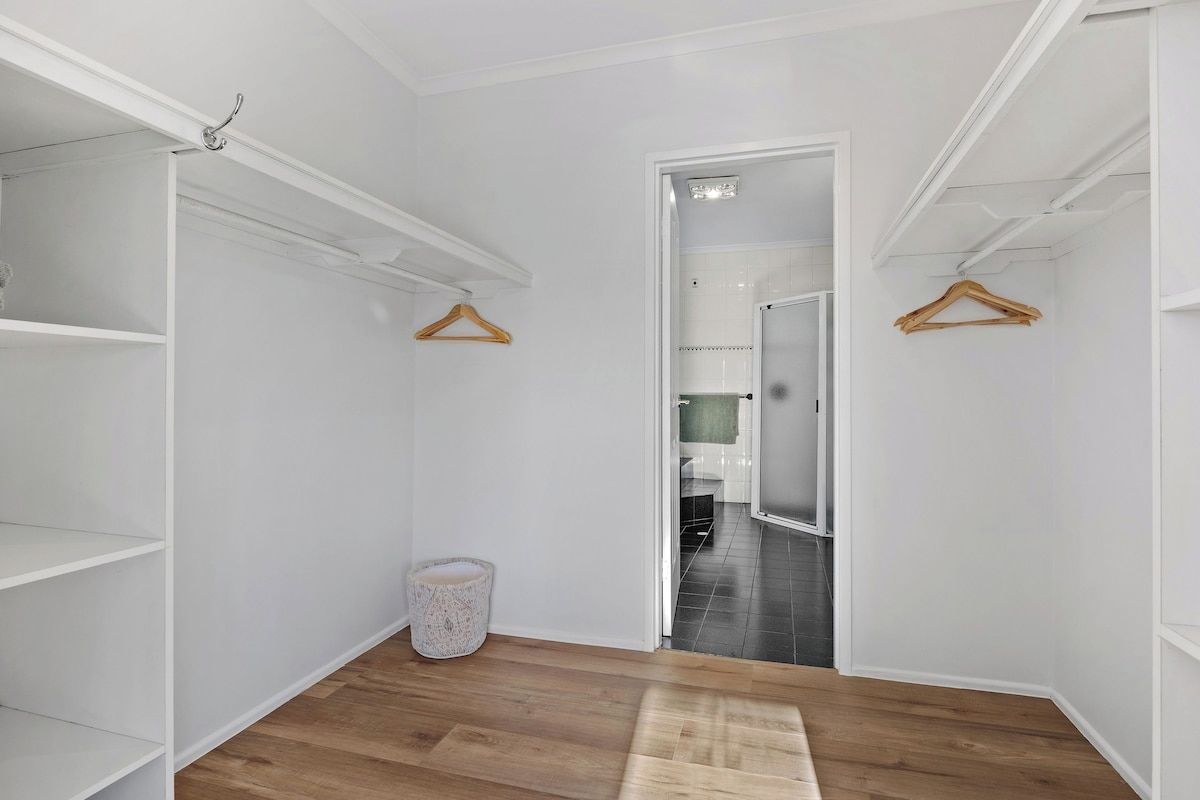 A hallway with white walls, wooden flooring, and a door leading to a bathroom.