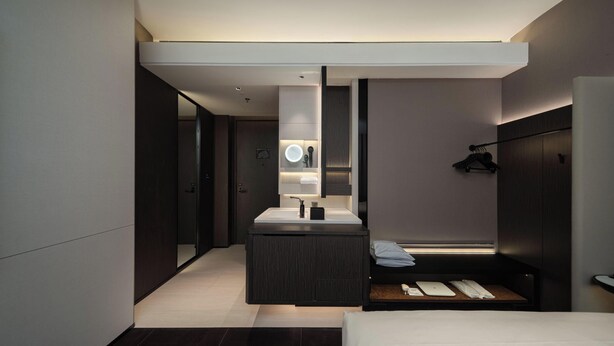 A modern hotel room with a central sink, a mirror, a bedside table, and a wardrobe.