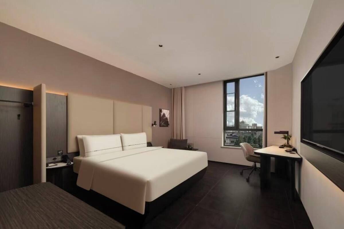 Ein modernes Hotelzimmer mit einem großen Bett, einem Schreibtisch, einem Sessel und einem großen Fenster mit Blick auf die Stadt.
