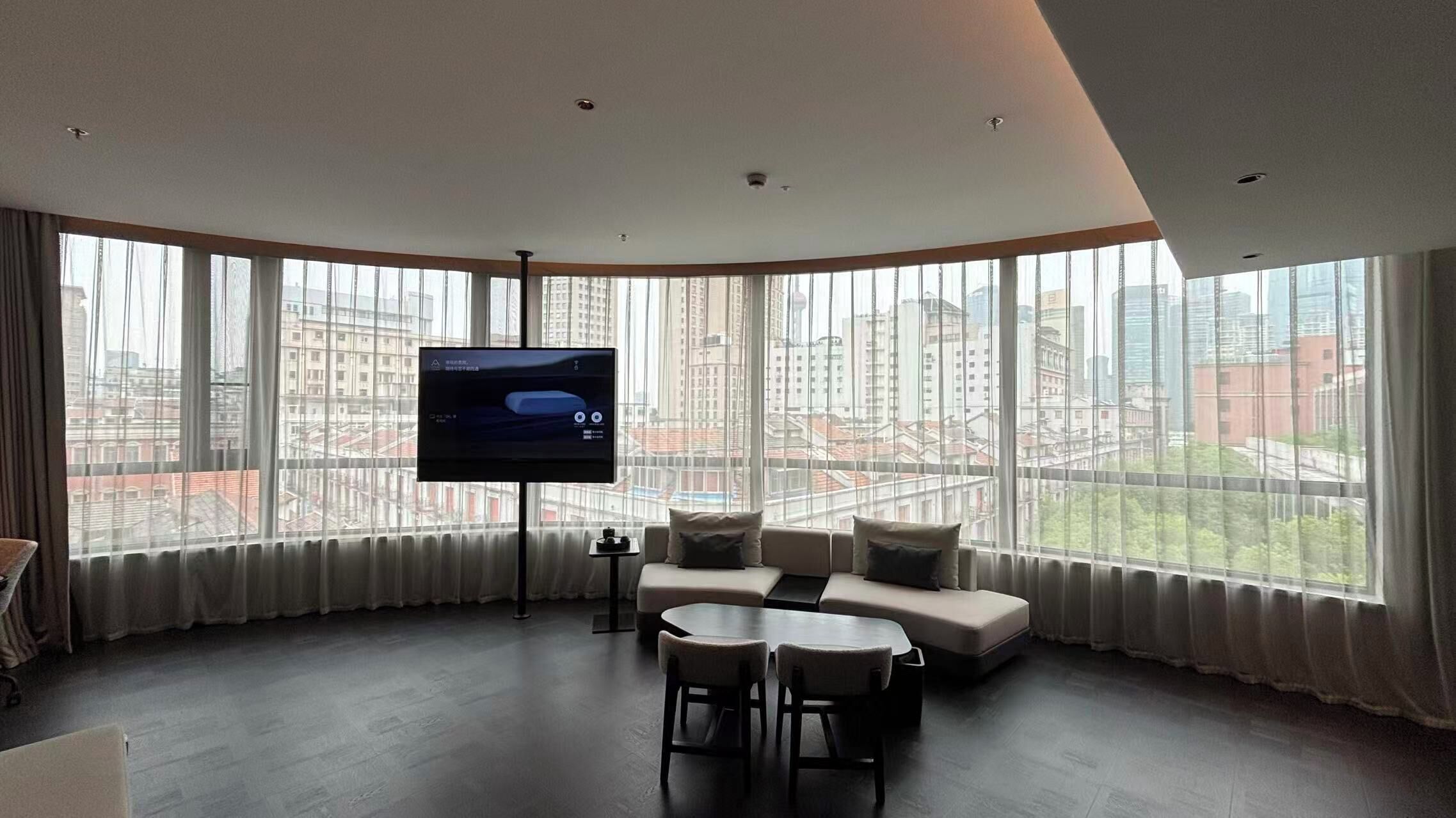 A modern living room with a large TV, comfortable seating, and a city view.