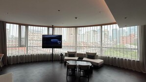 A modern living room with a large TV, comfortable seating, and a city view.