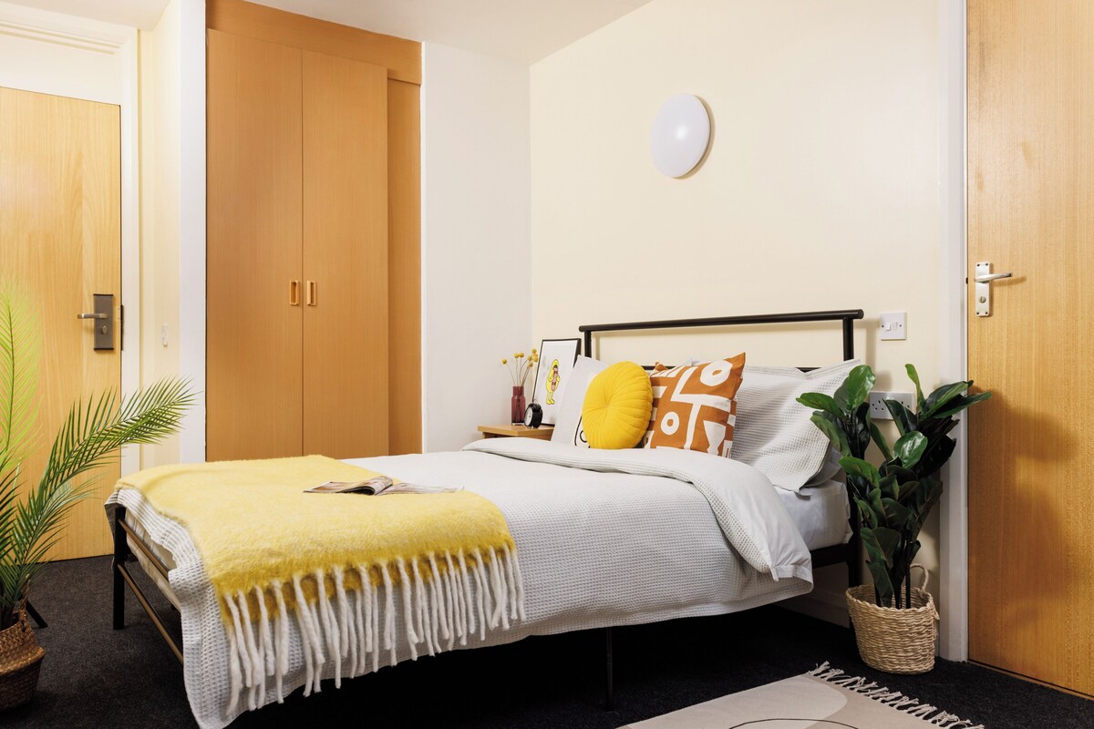 Ein Schlafzimmer mit Bett, Nachttisch, Lampe und einer Topfpflanze.