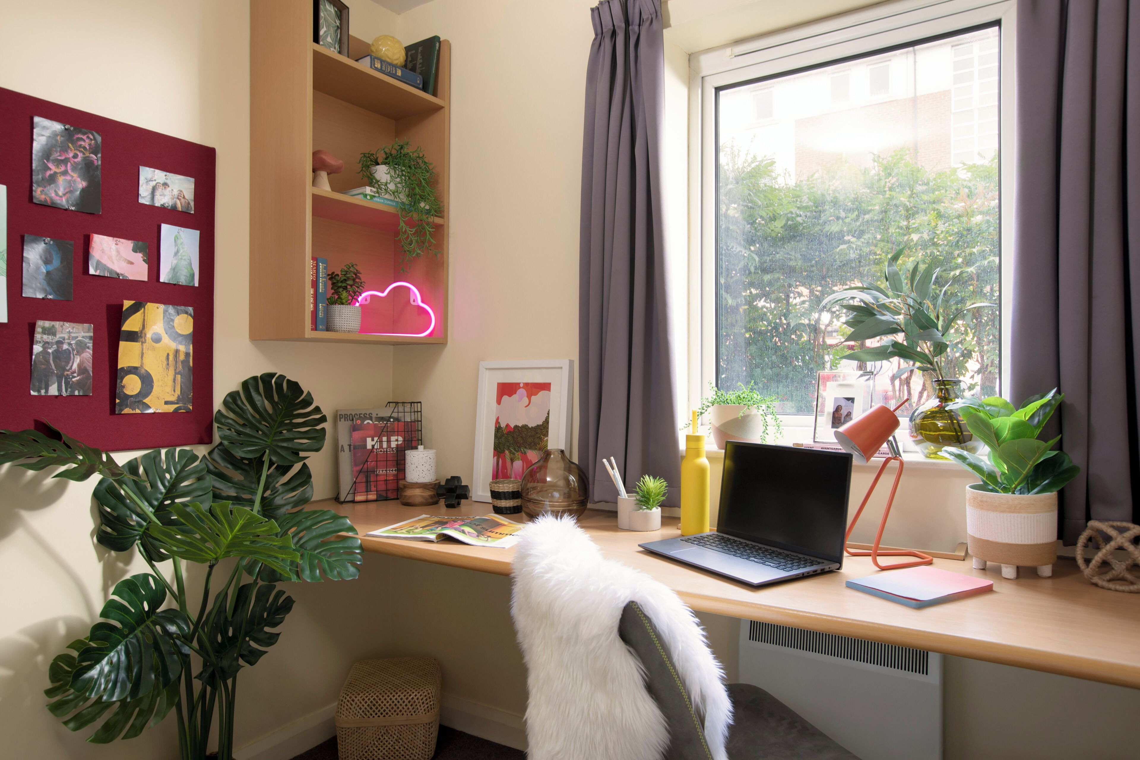 A workspace with a laptop, a desk lamp, a notebook, and potted plants.