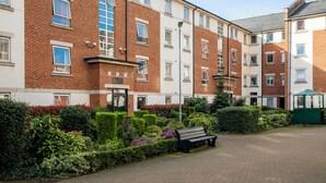 En flervåningsbostadsbyggnad med en fasad av tegel, en liten trädgårdsyta med en bänk och en grön konstruktion.