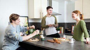Ett modernt kök med en matplats, där man ser en bänkskiva med matvaror, en kaffemugg och en person som håller i en tallrik.