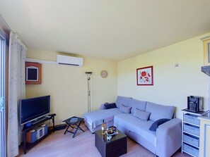 A living room with a TV, sofa, coffee table, and a wall-mounted air conditioner. - Tennis Résidence by Interhome (Saint Cyprien)
