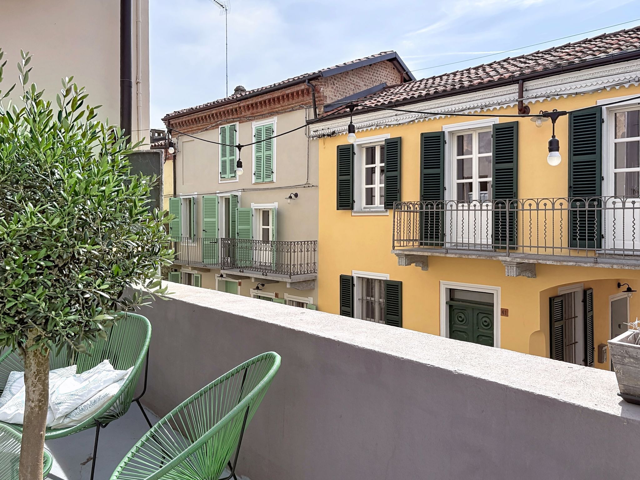 Un balcon avec une chaise verte, un pot de fleurs et un bâtiment jaune aux volets verts.