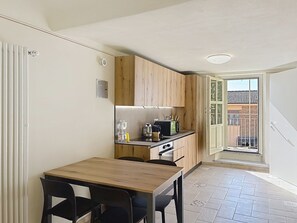 Cocina compacta con armarios de madera, una mesa de comedor con sillas y vistas a un área exterior por una puerta abierta.