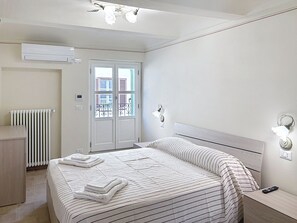 A modern hotel room with a bed, a radiator, an air conditioning unit, a bedside table with a remote control, and a view through a glass door. - Il Borghetto di Castagnole by Interhome (Castagnole Monferrato)