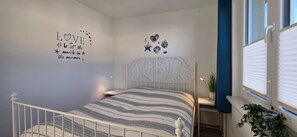 Een slaapkamer met een bed, een muur met een motiverende quote, een raam met jaloezieën en een klein plantje op de vensterbank.