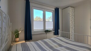 Un dormitorio con cama, ventana con cortinas, una planta en maceta y un armario.