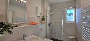 Een moderne badkamer met een grote spiegel, een wastafel, een douche en een klein raam.