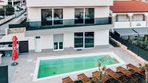 Un bâtiment moderne à deux étages, doté d’une piscine et d’un espace extérieur aménagé pour s’asseoir.
