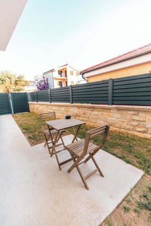 An outdoor patio with a table and chairs, a stone wall, and a building in the background. - Villa Aura Vir (Vir)
