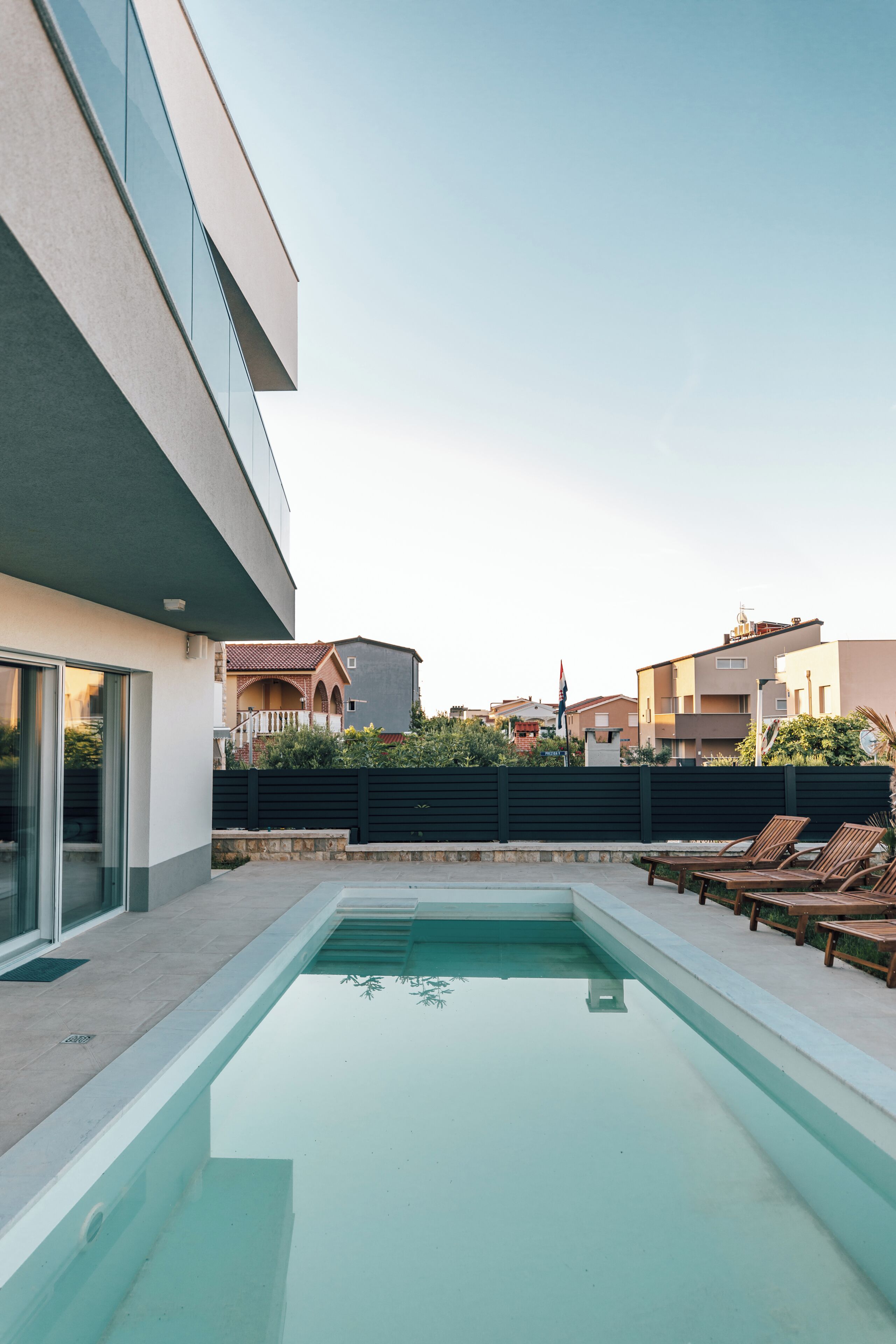 A swimming pool with lounge chairs, a modern building, and a clear sky.