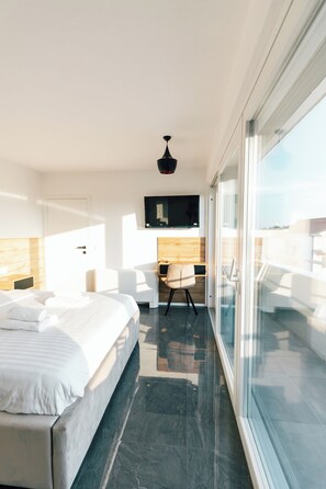 A modern hotel room with a bed, a desk, a chair, a TV, and a balcony with a glass wall. - Villa Aura Vir (Vir)