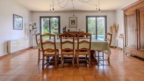 A dining area with a table set for six, wooden chairs, a chandelier, and a view through large windows.
