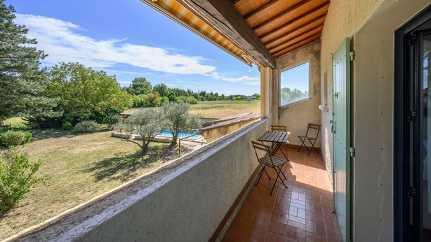 A balcony with a view of a swimming pool, green trees, and a clear sky.