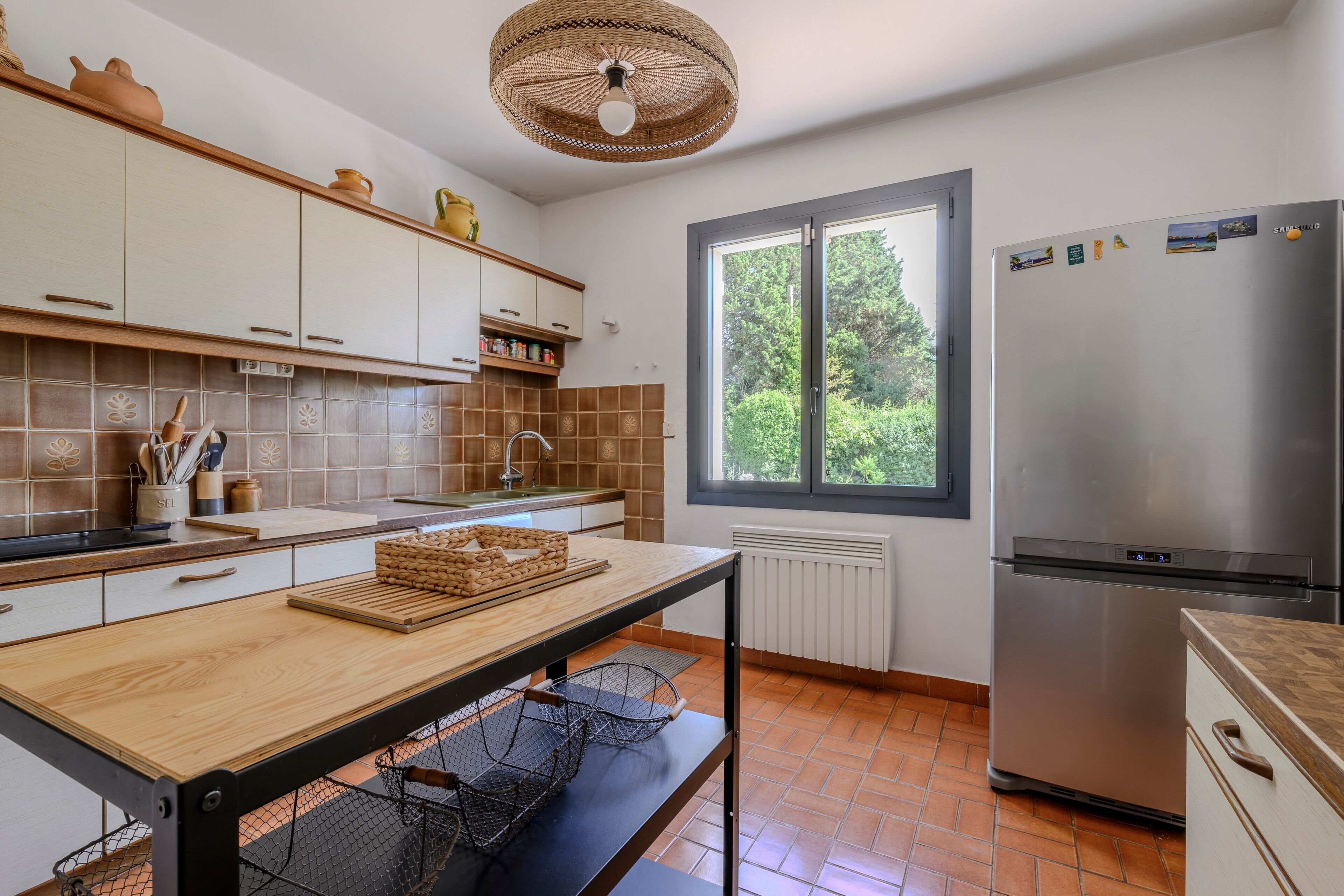 A kitchen with a large window, a stainless steel refrigerator, and a wooden table.