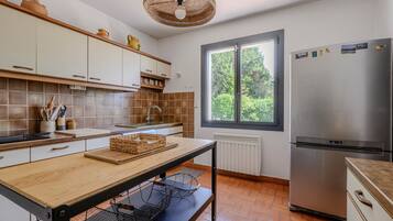 A kitchen with a large window, a stainless steel refrigerator, and a wooden table.