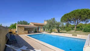 A swimming pool with lounge chairs, a patio area, and a building with a tiled roof.