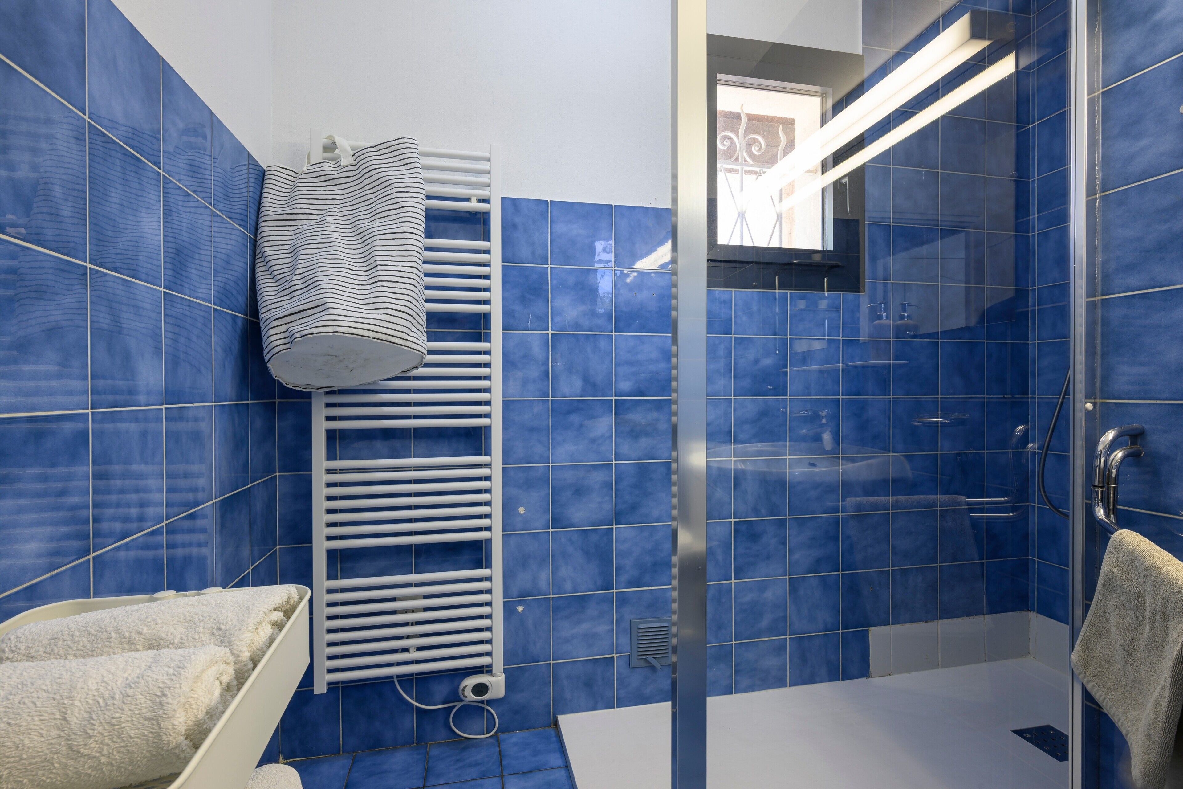 A bathroom with blue tiles, a white towel rack, a shower area, and a glass door.