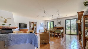 A spacious living area with a television, wicker furniture, a fireplace, and large windows.