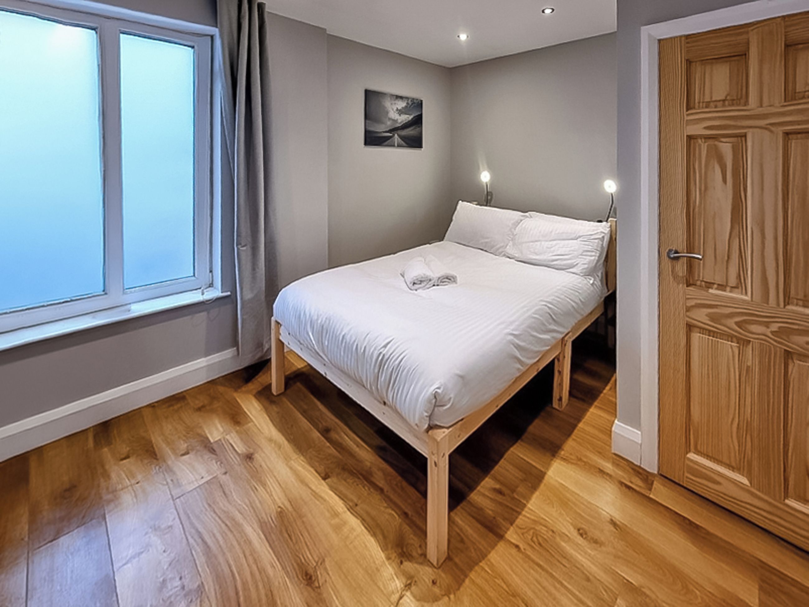 A bedroom with a bed, a window, a door, and a painting on the wall.