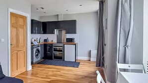 Een kleine keuken met apparatuur, een wasmachine en een eethoek met een tafel en stoelen.
