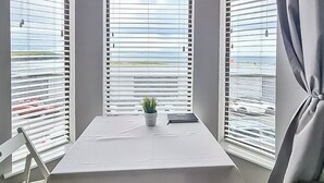 Een hotelkamer met een tafel, stoelen, een potplant en ramen met jaloezieën.