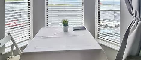 A hotel room with a table, chairs, a potted plant, and windows with blinds.